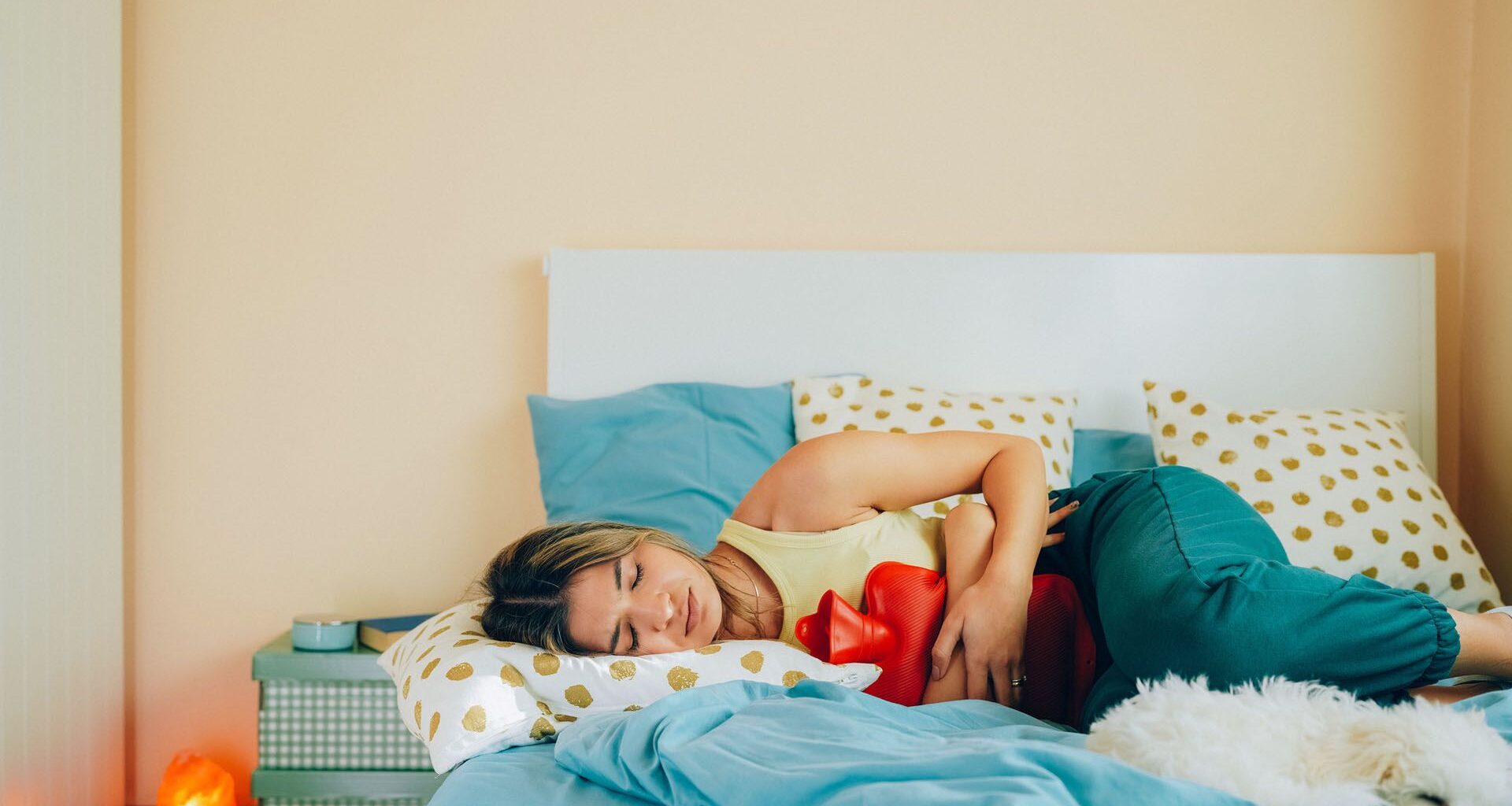 woman laying on her bed holding a hot water bottle to her stomach