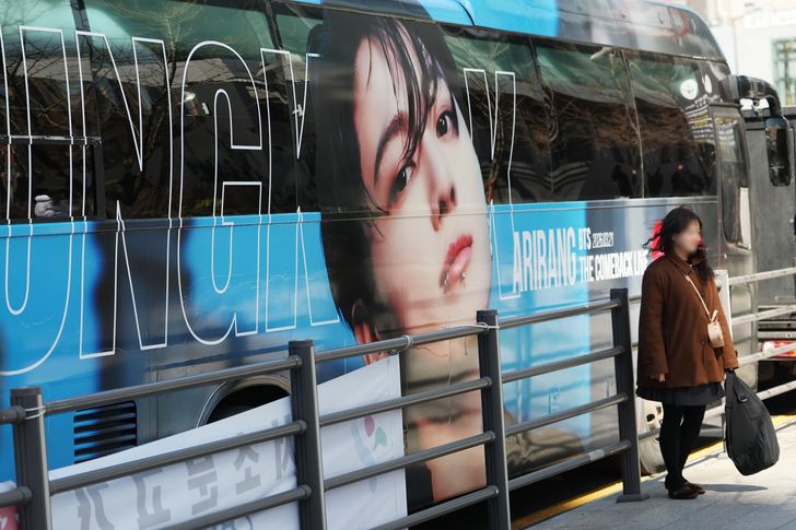 Ahead of BTS’ Gwanghwamun performance, a fan poses in front of a bus decorated with the image of member Jung Kook, near the HYBE building in Yongsan District, Seoul. Yonhap