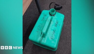 A green petrol can marked with the words 'bike neat' in pen placed on a carpet