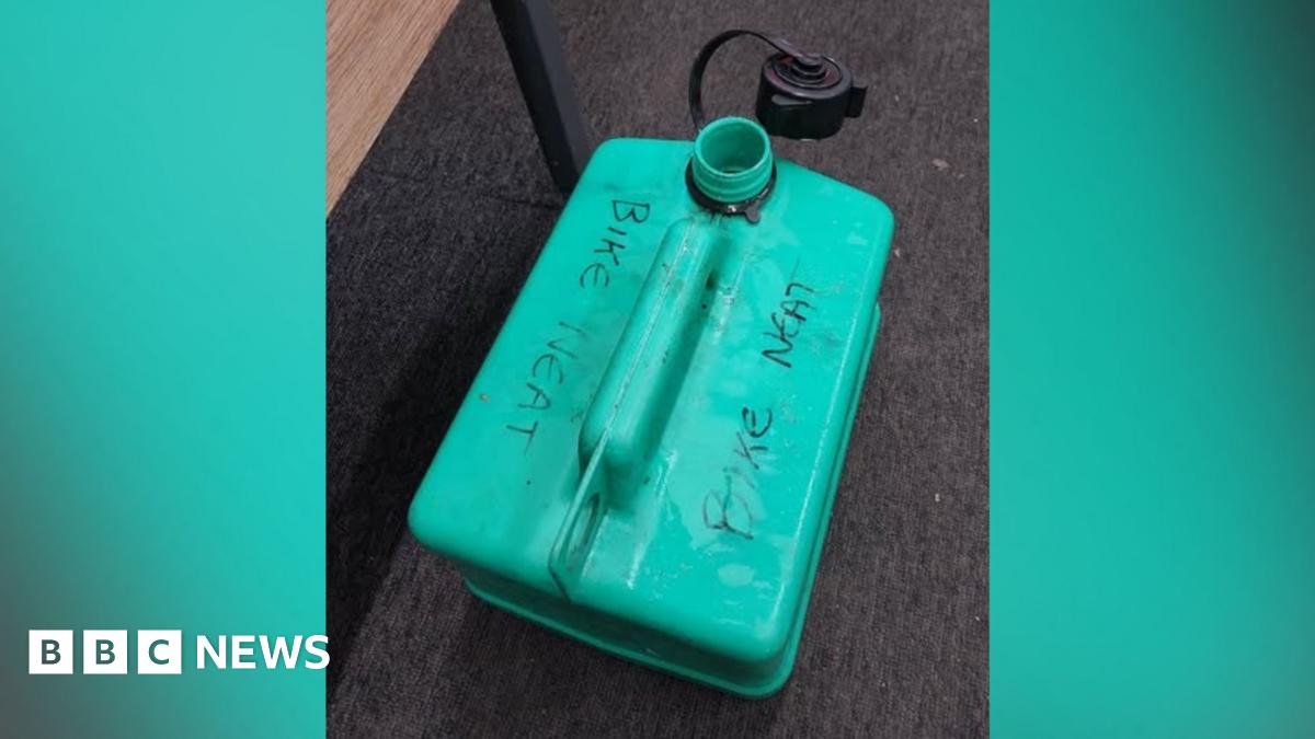 A green petrol can marked with the words 'bike neat' in pen placed on a carpet