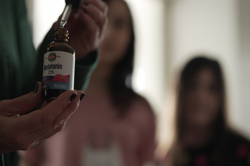 Woman holds bottle of melatonin with two children in the background.