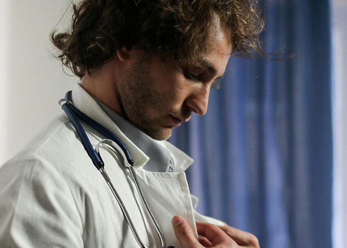 Young male doctor with stethoscope adjusting his coat, reflecting the medical secrets so dark theme in a clinical setting.