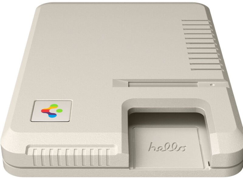 A beige, retro-styled computer case with minimal features, a colorful logo button on the left, vent slits on the right, and a "hello" label above a rectangular slot at the bottom front.