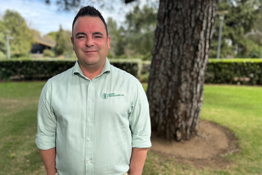 A man in a light green business shirt stands towards the camera with his hands in his pockets.