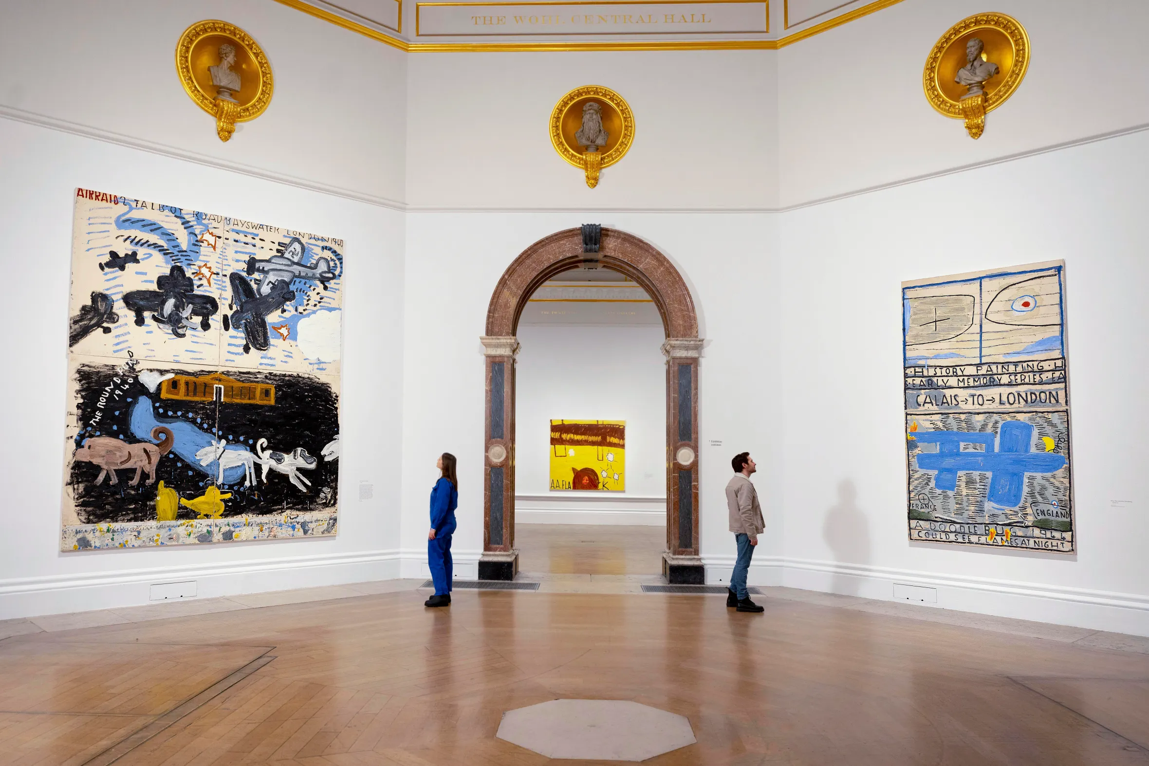 Visitors viewing Rose Wylie's paintings "Airraid Talbot Road Bayswater London 1940" and "Calais to London (A Doodle Bug 1944)" at the Royal Academy of Arts.