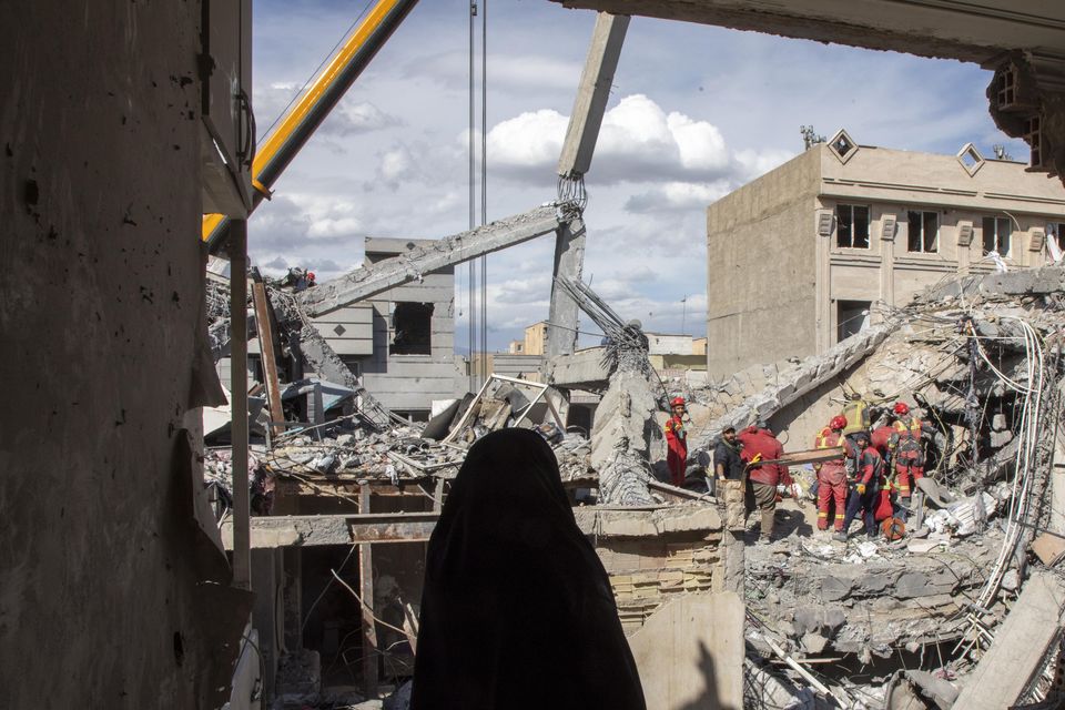 A woman looks on as residents and emergency workers sift through rubble of a residential building that was hit in an airstrike in the early hours of March 27 in Tehran, Iran. Photo: Getty
