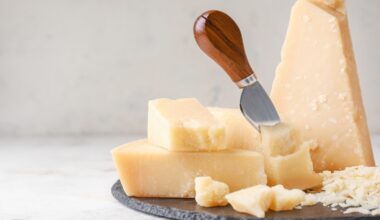 Close up of Parmesan cheese wedges and shavings on a serving board with a cheese knife.