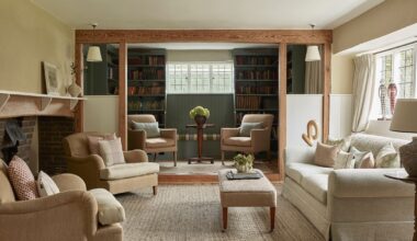 Country cottage living room with cream sofa, beige armchairs, large brick fireplace, green painted library with bookshelves and two armchairs