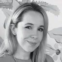 A woman with light hair smiling at the camera, with a floral background in grayscale.