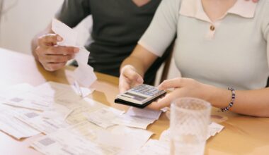A man and woman seated at a table with papers, bills, receipts, and a calculator in front of them