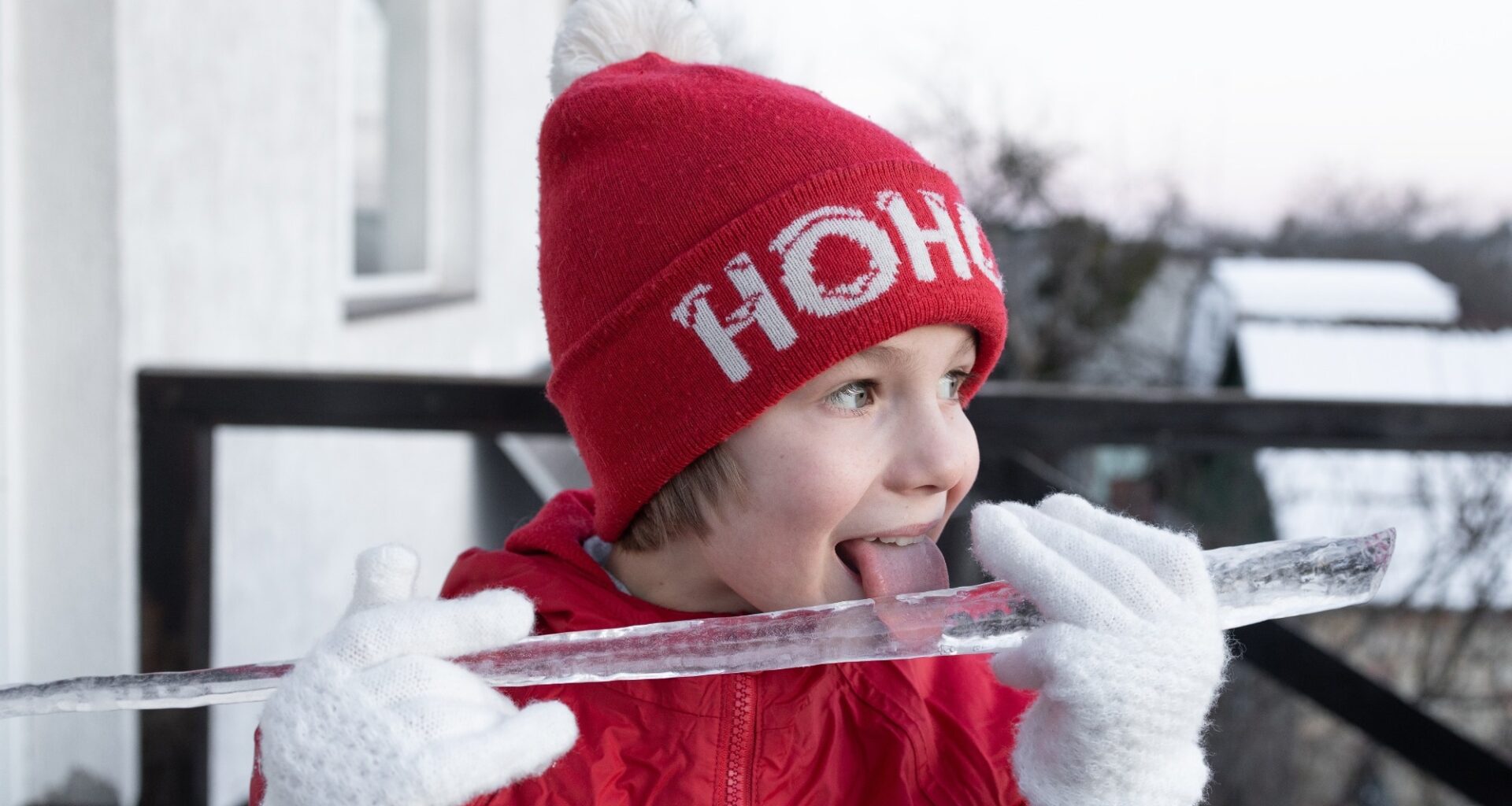 boy plays with a large icicle in winter, happily tasting it with his tongue hanging out.