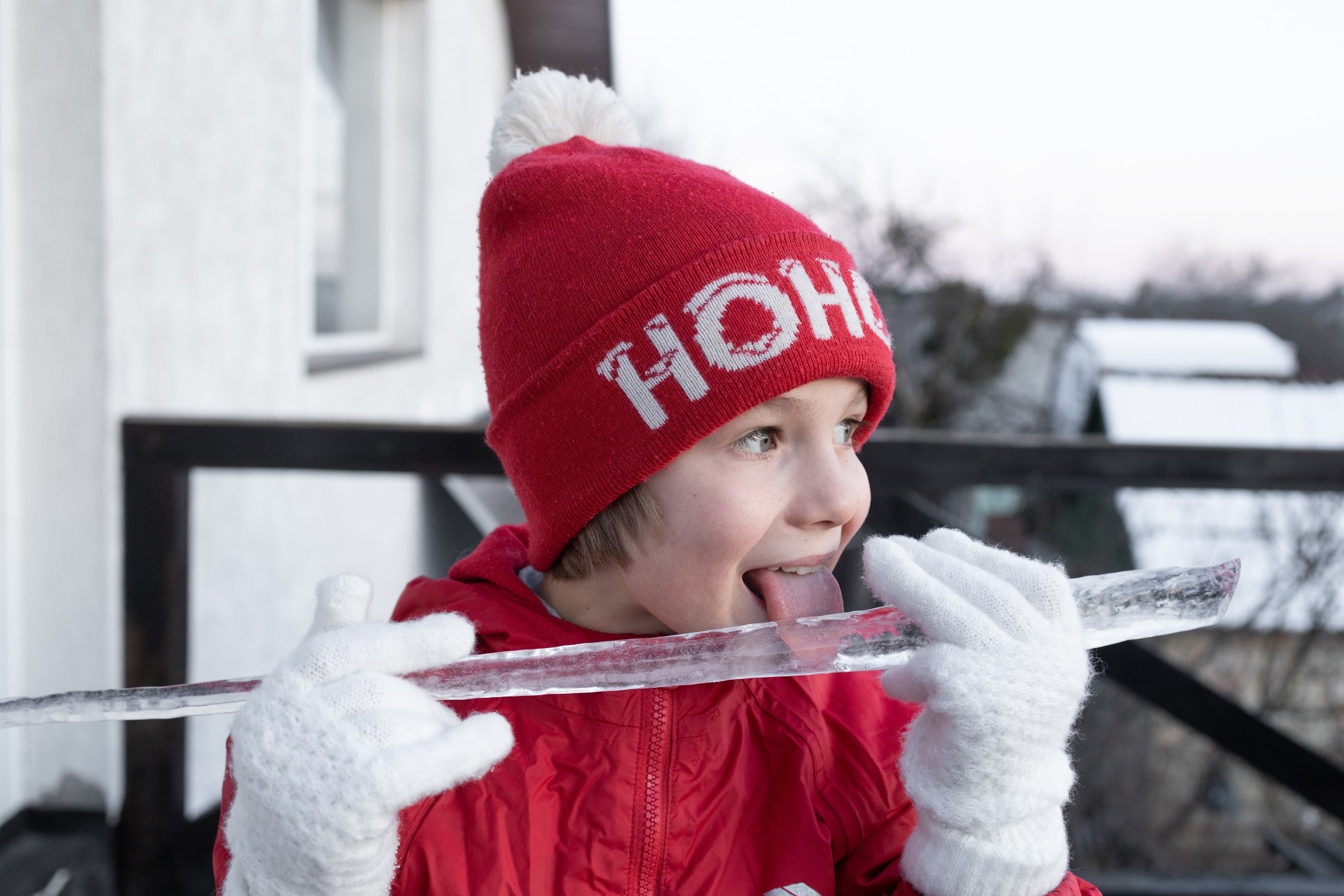 boy plays with a large icicle in winter, happily tasting it with his tongue hanging out.