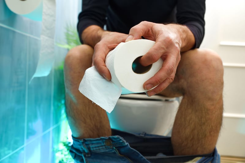 A man sitting on a toilet holding toilet paper