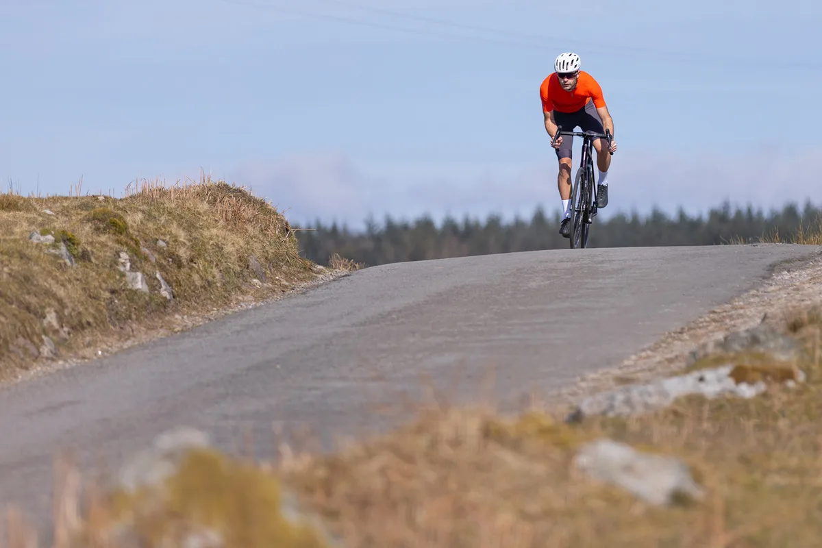 Male cyyclist in orange top riding the Orbea Orca M20i Team road bike
