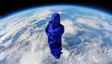 A figure draped in flowing blue fabric floats above Earth, with the planet’s clouds and atmosphere visible below, creating a surreal and dreamlike scene as viewed from space.