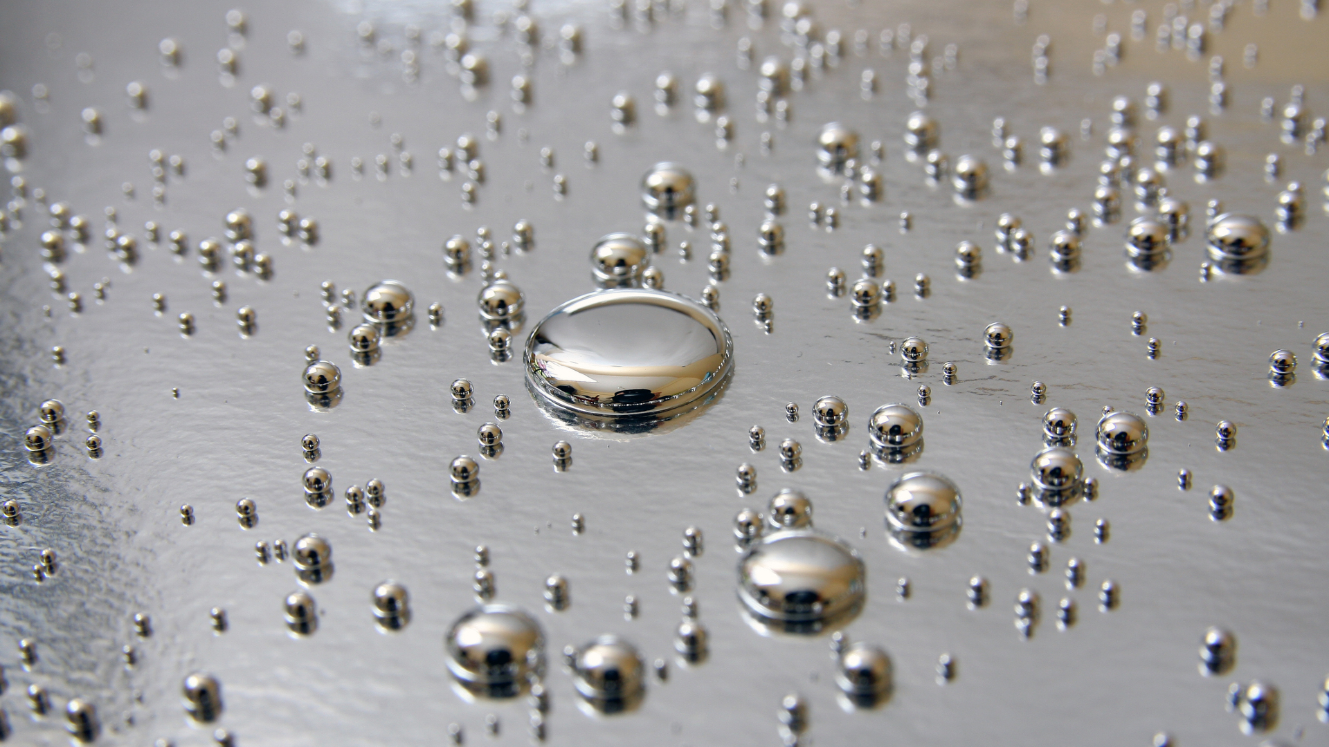 A series of silver circular droplets shine against a silvery metal surface