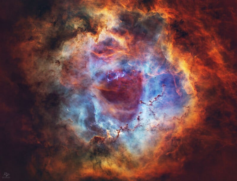 Bright, colorful nebula in space with swirling clouds of blue, red, orange, and yellow gases, forming a circular shape with a dark center surrounded by vibrant, glowing light.