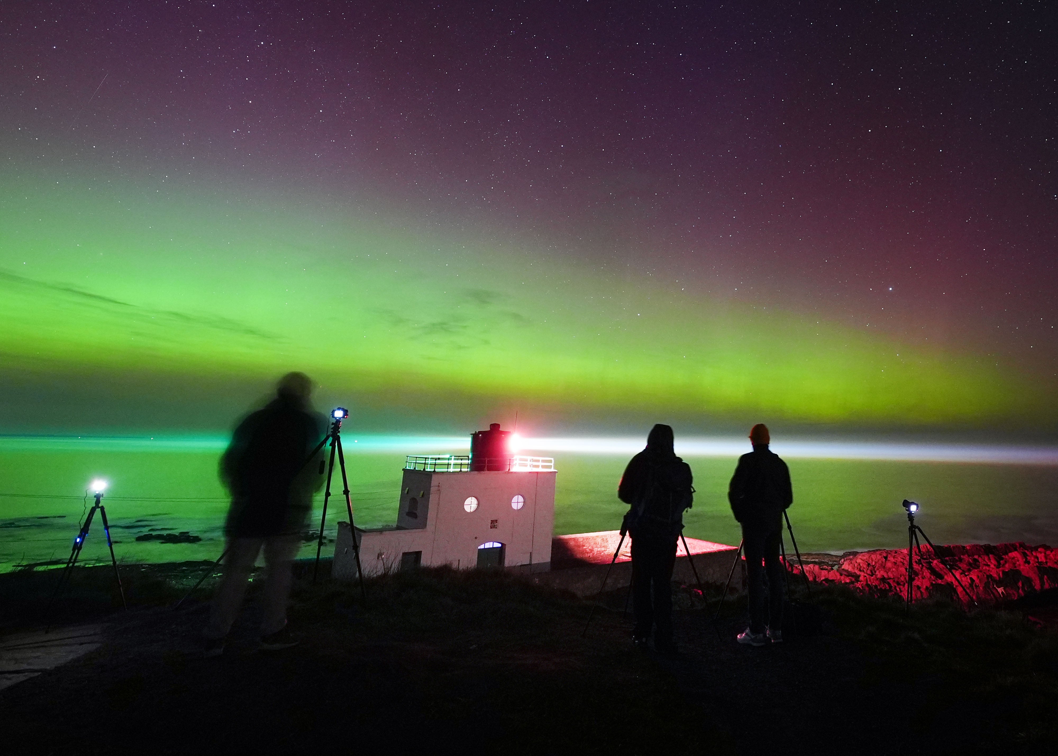 Photographers and stargazers watch as the aurora borealis, commonly known as the Northern Lights, light up the skies above Bamburgh lighthouse in Northumberland