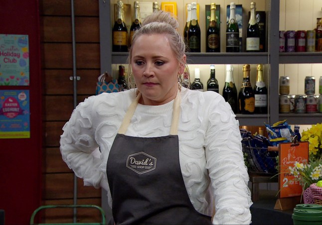 Amy Walsh stood in the shop in Emmerdale, wearing an apron