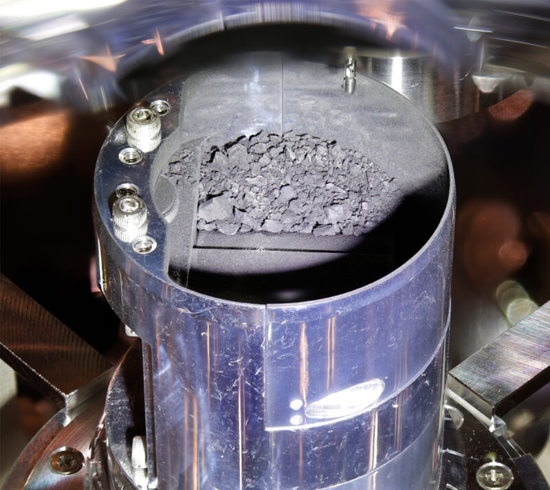 Life’s genetic code: Small chips of gray gravel and dust inside a blue metal cylinder.