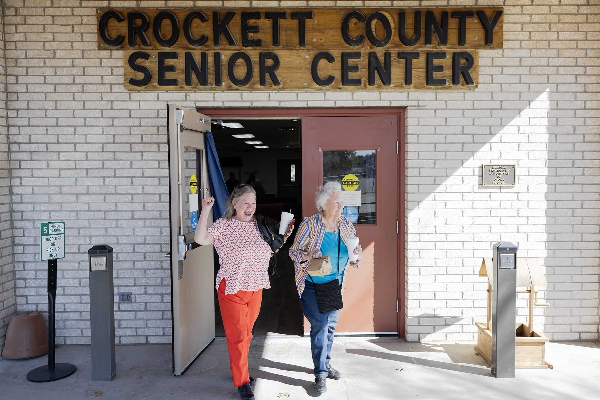 Two older women walk gleefully out of a building labeled Crockett County Senior Center