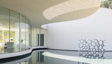 Modern architectural design with curved glass walls and a honeycomb-like sculpture by a reflective water surface.