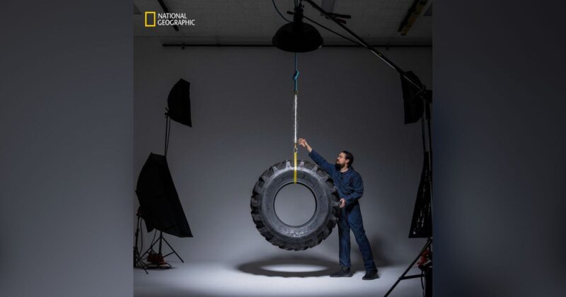 A man in a studio setting stands next to a large tire hanging from the ceiling by a rope. He is touching the tire, and professional lighting equipment is visible around him. The National Geographic logo appears in the top left corner.