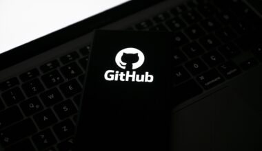 GitHub logo pictured on a smartphone placed on top of a laptop keyboard, with blank white screen in corner.
