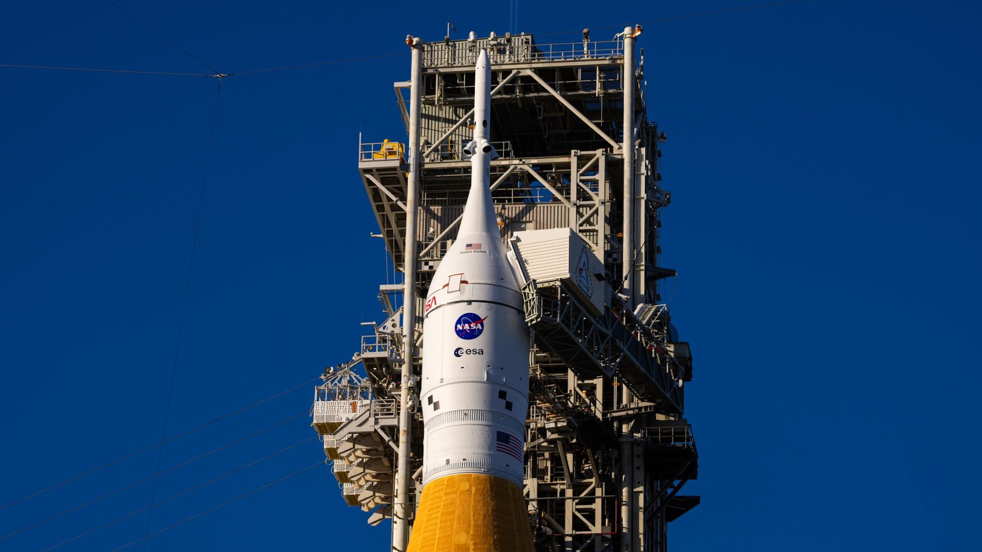 closeup of a white space capsule atop an orange rocket on the launch pad