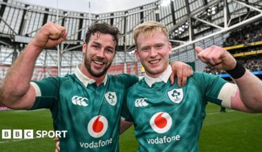 Caelan Doris and Jamie Osborne in a celebratory pose, arm in arm, with each man raising a clenched fist and smiling, while wearing Ireland's green shirt
