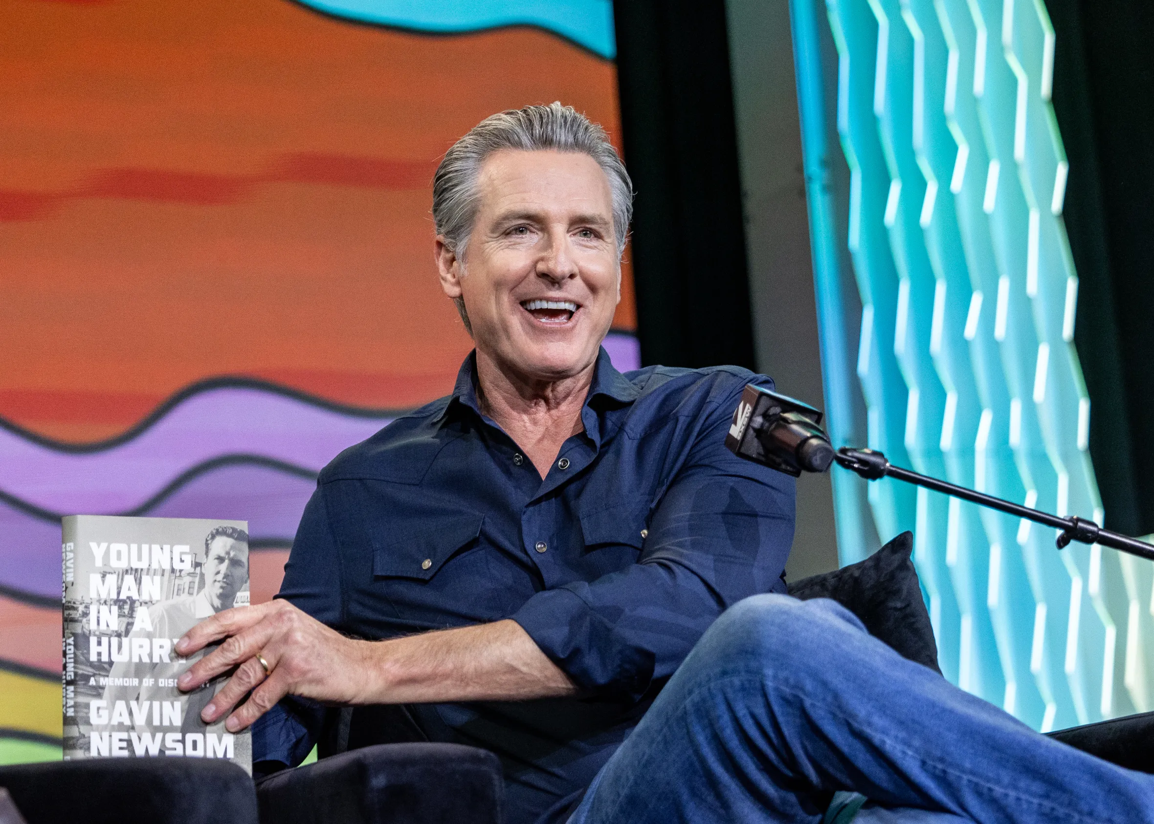 Governor Gavin Newsom smiling and holding his book "Young Man in a Hurry" at the SXSW Conference.