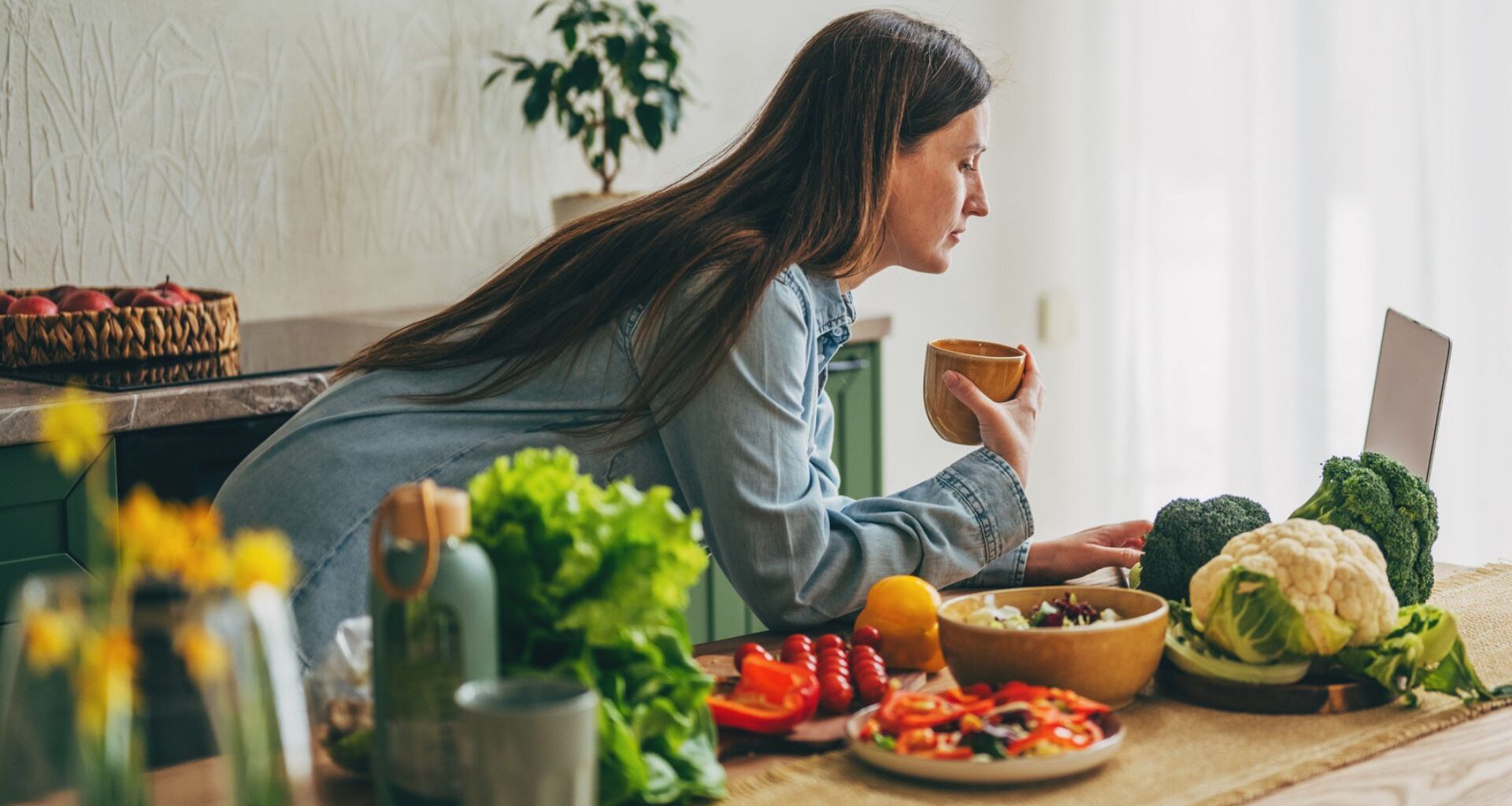 woman looks at laptop while surrounded by healthy foods in her kitchen