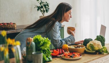 woman looks at laptop while surrounded by healthy foods in her kitchen