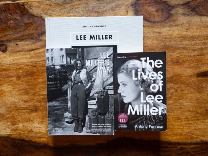 Three books about Lee Miller are displayed on a wooden surface. The covers feature black-and-white portraits of Miller and titles: "LEE MILLER," "LEE MILLER'S WAR," and "The Lives of Lee Miller.