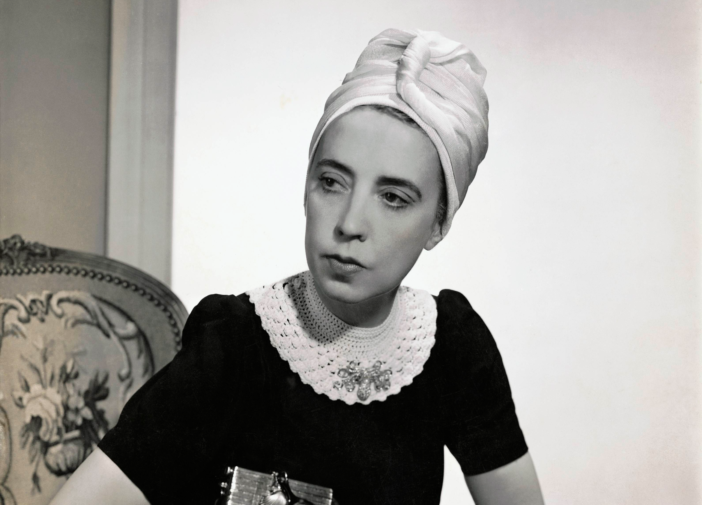 Designer Elsa Schiaparelli wearing a black silk dress with a crocheted collar and white turban.