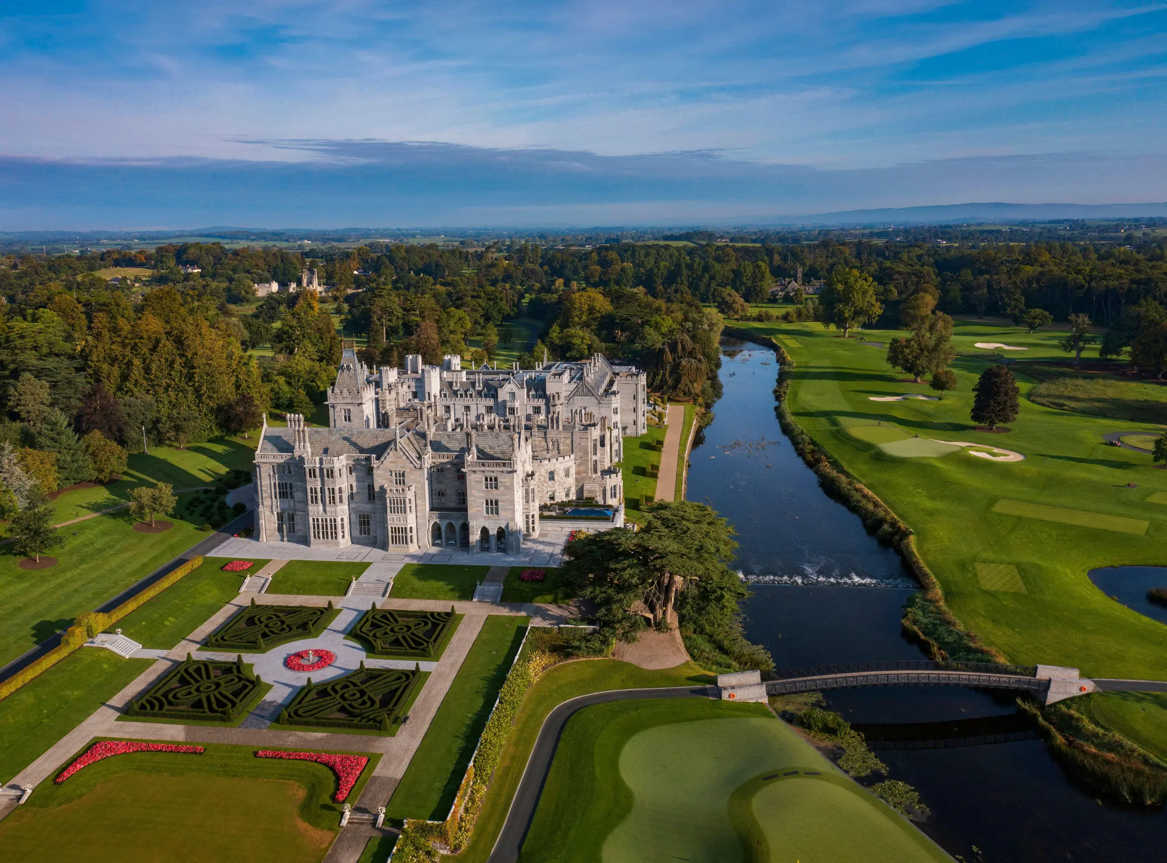 Aerial view of Adare Manor Hotel and Golf Resort with manicured grounds, a river, and golf course.