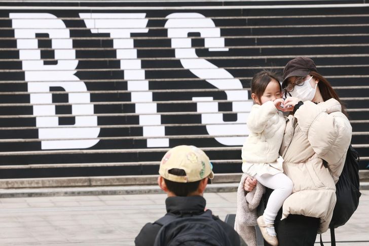 A family of foreign tourists poses in front of a promotional ad for a concert by K-pop boy band BTS, on the steps of the Sejong Center for the Performing Arts in Jongno District, Seoul, March 11. Yonhap