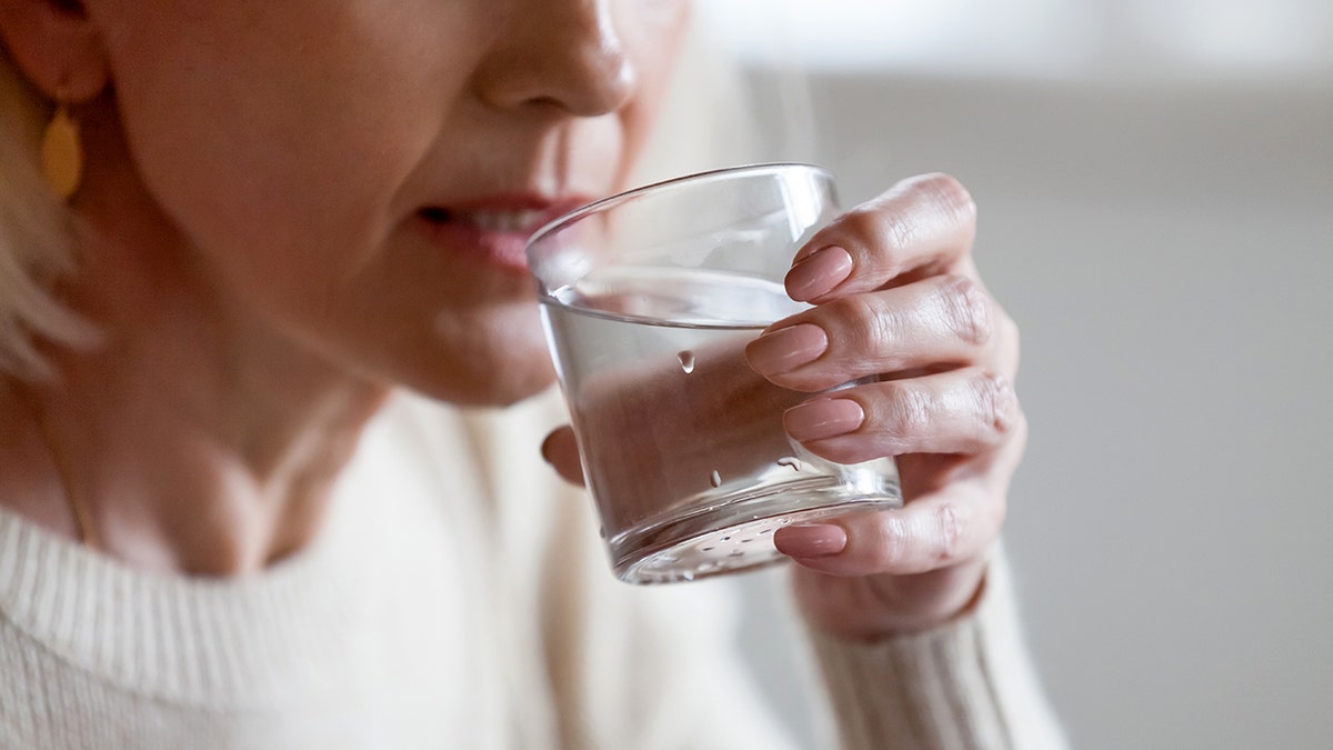 Drinking fresh water from a glass, a woman raising the glass to her lips