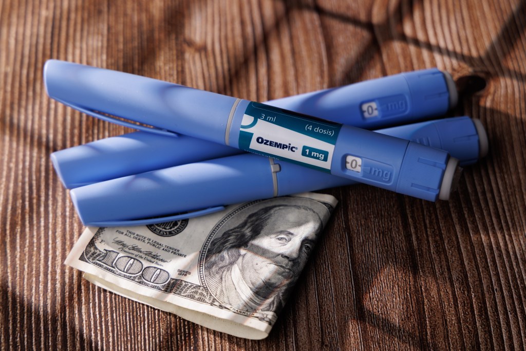 Blue Ozempic semaglutide injection pens resting on $100 bill, symbolizing the high cost of weight-loss therapy