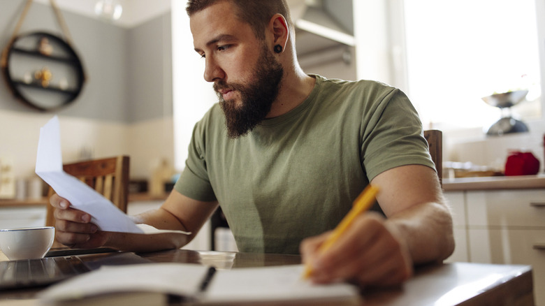 Bearded man with ear piercing looks over documents while sitting at table