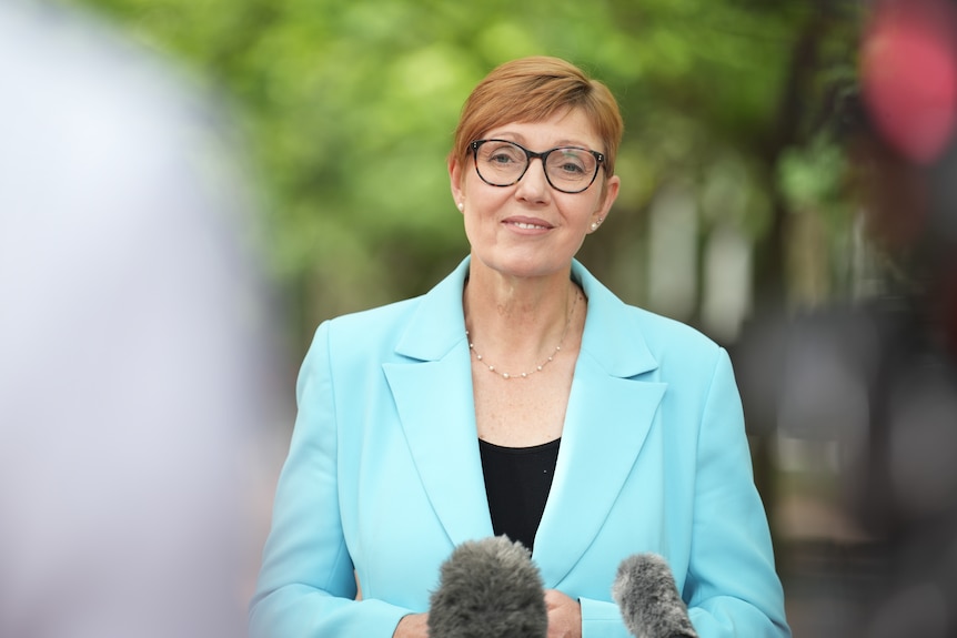 Rachel stands outside in a pale blue blazer and smiles.