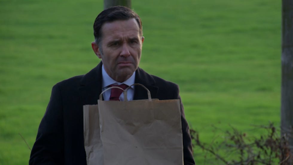 man holding a paper bag standing outdoors in a green field