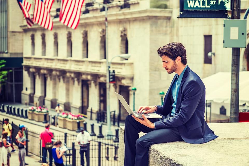 A person sitting in front of a Wall Street sign.