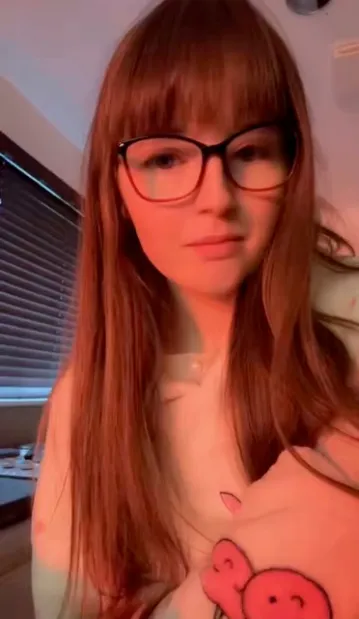 Charlotte Clerk, a young woman with long reddish-brown hair and glasses, looks toward the camera.