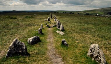 A view of lush rolling hills under a cloudy gray sky. In the foreground is a faded narrow dirt road with stones on either side of it