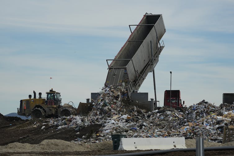 A large truck dumps trash in a massive pile.