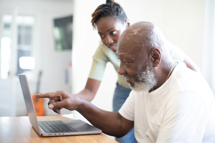 A man with a greying beard pointing at a laptop screen while a younger woman looks over his shoulder