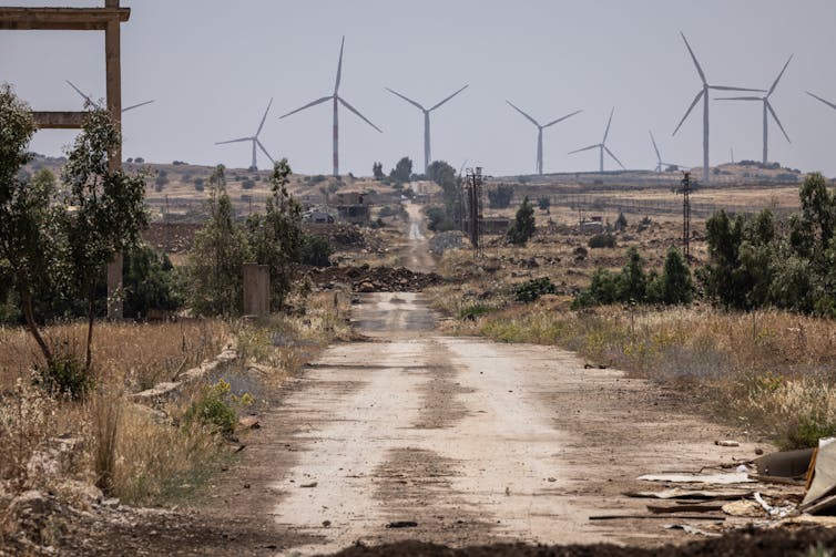 A view down a dusty road, with wind turbines in the distance.