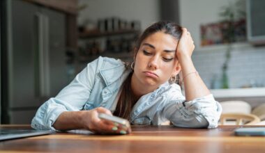 An annoyed woman leans on a table and looks at her phone.