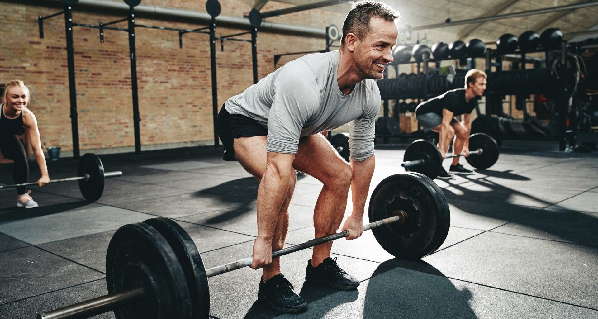 Three people doing a barbell deadlift during gym workout
